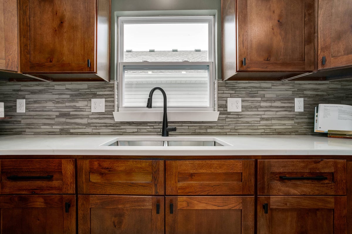 Modern kitchen sink with a large window, elegant black faucet, and wood cabinetry